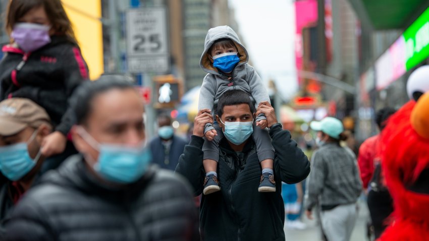 A child wearing a mask sits on his father's shoulders while walking through Times Square