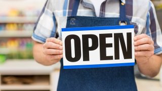 File image of a grocery store worker holding an 'open' sign.