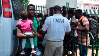 Un grupo de migrantes junto a una camioneta aguardan para ingresar a una sede migratoria en México, donde deberán demostrar su estancia legal en el país.