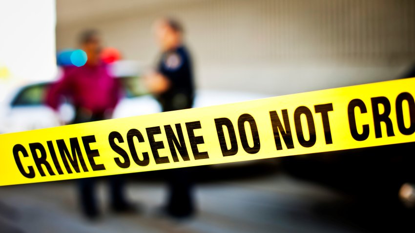 Closeup of crime scene tape with police officers and police car in background.