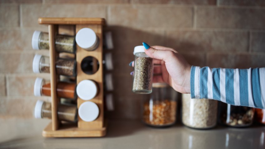 Cropped hand holding jar of spices on kitchen counter.