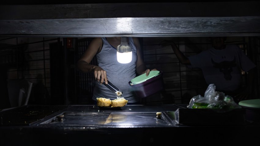 Una persona vende comida ayudado con un bombillo en medio de la oscuridad durante un corte eléctrico, el 29 de febrero de 2024 en Maracaibo (Venezuela). EFE/ Henry Chirinos