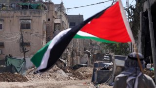 Un hombre sostiene una bandera palestina mientras soldados israelíes realizan una operación en el campo de refugiados de Tulkarem, cerca de la ciudad cisjordana de Tulkarem, este miércoles. Al menos dos palestinos murieron el 10 de septiembre durante las operaciones militares israelíes en Tulkarem y su campo de refugiados, según el Ministerio de Salud palestino.