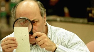 El juez Robert Rosenberg de la Junta de Escrutinio del Condado de Broward utiliza una lupa para examinar una marca de papeleta perforada el 24 de noviembre de 2000 durante un recuento de votos en Fort Lauderdale, Florida.