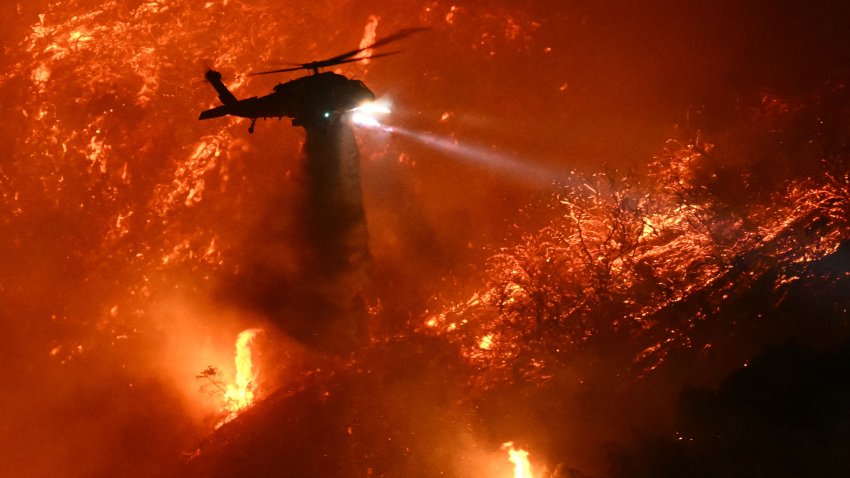 A fire fighting helicopter drops water as the Palisades fire grows near the Mandeville Canyon neighborhood and Encino, California, on January 11, 2025. The Palisades Fire, the largest of the Los Angeles fires, spread toward previously untouched neighborhoods January 11, forcing new evacuations and dimming hopes that the disaster was coming under control. Across the city, at least 11 people have died as multiple fires have ripped through residential areas since January 7, razing thousands of homes in destruction that US President Joe Biden likened to a “war scene.” (Photo by Patrick T. Fallon / AFP) (Photo by PATRICK T. FALLON/AFP via Getty Images)