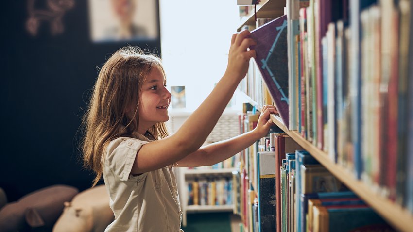 Schoolgirl choosing book in school library. Smart girl selecting literature for reading. Books on shelves in bookstore. Learning from books. School education. Benefits of everyday reading