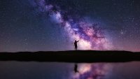 Person pointing up the Milky Way galaxy at night. The scene is reflected in water. A Veiga, Ourense, Spain